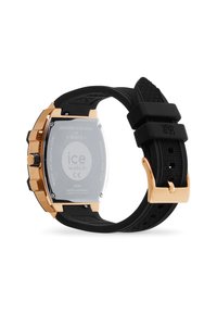 Montre à bracelet en caoutchouc noir avec un boîtier en acier inoxydable doré, de forme arrondie, bande texturée et mouvement de montre visible à l'arrière.