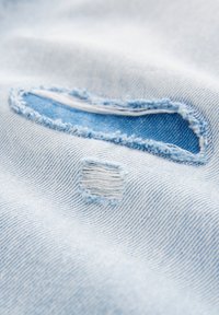 Lyseblåt denimstof med frynser: et rektangulært og et ovalt lap, med synlige tråde og struktur.