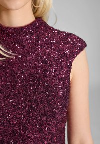 Fuksjowa bluzka z cekinami o wysokiej szyi i krótkich rękawach, charakteryzująca się teksturowaną, błyszczącą powierzchnią wykonaną z licznych małych cekinów.