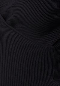 Svart ribbad tygblus med texturerad yta och böjd sömmönster, med vertikala ränder och en tight passform.