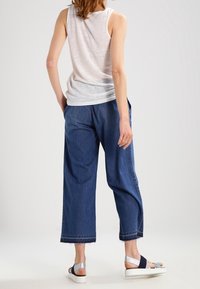 Haut blanc sans manches avec une coupe décontractée ; pantalons en denim bleu clair à jambes larges ; et chaussures avec une bride marine et des accents argentés.