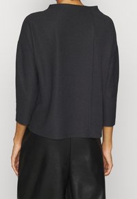 Maglione nero a coste con una texture morbida, caratterizzato da una vestibilità ampia e maniche a tre quarti, con collo alto e dettaglio di cucitura sul retro.