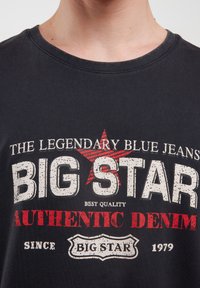 Juodas medvilninis marškinėlis su balta ir raudona grafika. Tekstas apima "BIG STAR" ir "AUTHENTIC DENIM" su žvaigždute.