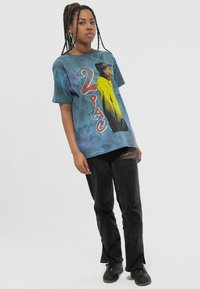 Tie-dye t-shirt featuring a colorful 2Pac graphic, short sleeves, relaxed fit. Paired with black jeans and dark sneakers.