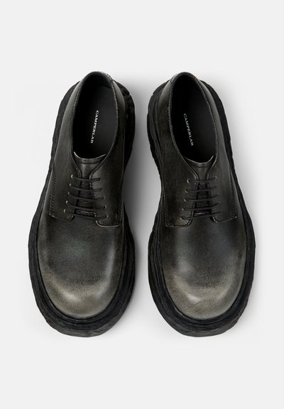 Pari mustia nahkaisia nyörikenkiä, joissa on paksut ja kuvioidut pohjat, nähtynä ylhäältä valkoisella taustalla.