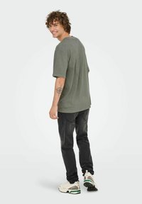Grå oversized t-shirt med korte ærmer, parret med sorte jeans og lyse sneakers med grønne detaljer. Tattoo synlig på armen.