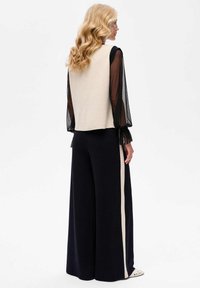 Beige mouwloos topje gecombineerd met marineblauwe wijde broek met een verticale crèmekleurige streep. Doorzichtige zwarte lange mouwen met gerimpelde manchetten.