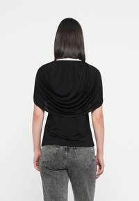 Schwarzes drapiertes Oberteil mit kurzen Ärmeln, versehen mit einem gerafften Ausschnitt. Kombiniert mit grauen Jeans aus Denim, die eine verblasste Textur und fünf Taschen aufweisen.
