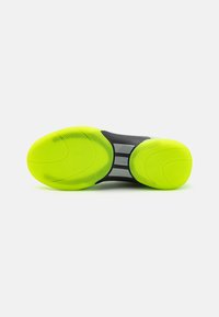Schwarze und neongrüne Laufsohle mit kreisförmigen Traktionsmustern und reflektierenden grauen Akzenten. Strukturiertes Gummi für besseren Grip.