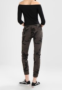 Kamouflagebyxor i mörka gröna och bruna nyanser, smalnande vid vristerna med elastiska muddar. Kombineras med en svart off-shoulder topp och svarta sneakers.