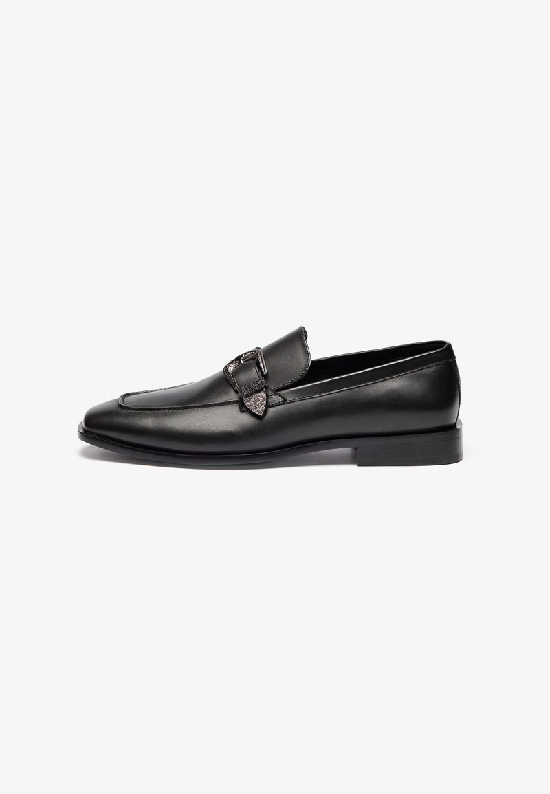 Mocasines de cuero negro con un diseño elegante, puntera puntiaguda y una hebilla decorativa en el lado lateral. Suela plana de goma y acabado pulido.
