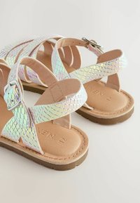 Sandali sintetici iridescenti, intrecciati, con cinturini incrociati, suola piatta marrone e un'accoppiatura argentata. Progettati con una finitura testurizzata.