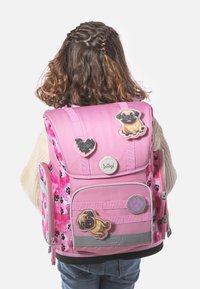 Zaino rosa con motivi a impronte di zampe, dettagli in pelliccia sintetica, diverse toppe tra cui un cuore e un design di carlino, e cinghie e hardware grigi.