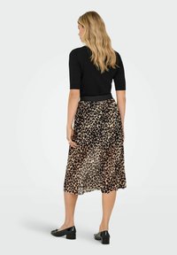 Melna īsām piedurknēm tops, kombinēts ar ceļa garuma leoparda raksta svārkiem ar plūstošu tekstūru un elastīgu jostu. Melnas plakanas kurpes noslēdz apģērbu.