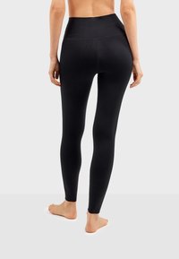 Leggings noirs taille haute avec une texture lisse et extensible. Présente un design sans couture sans couture visible ni matériel.