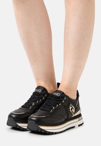 Sneaker in pelle nera con accenti dorati, design con lacci, suola bianca e nera e dettaglio del logo sul lato. Soprasso testurizzato e forma slanciata.