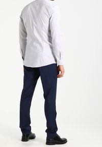 Une chemise bleu clair à manches longues avec une coupe droite, des poignets à boutons, et une texture lisse. Assortie à un pantalon tailored bleu foncé et des chaussures noires.