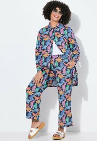 Farverigt, mønstret matchende sæt med en skjorte med knapper og løse bukser i blå, orange, grønne og lyserøde dyremotiver; stoffet ser let ud.