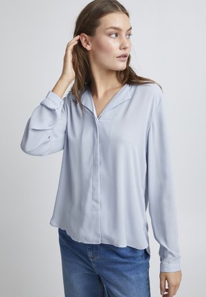 Light blue polyester blouse with a collar, long sleeves, and a slightly loose fit. Simple button closure, smooth texture, and minimal design.