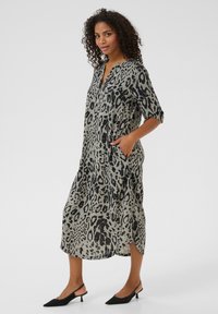 Robe midi imprimé animal en beige et noir, avec un col en v, des manches trois-quarts, des poches latérales et des fentes latérales pour faciliter les mouvements.