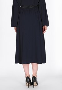 Marineblauwe jurk tot de knie met lange mouwen, getailleerde taille en zachte stof; gecombineerd met zwarte hoge hakken.