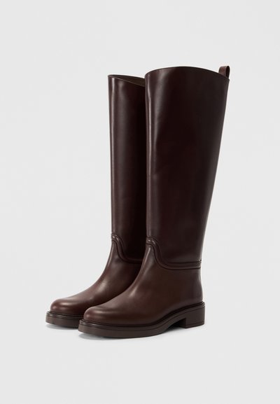 Bottes en cuir marron jusqu'au genou avec une finition lisse, bout rond et talon bloc. Elles présentent des coutures décoratives et une languette à l'arrière.