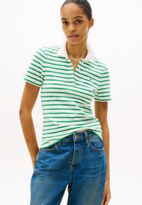 Πράσινο και λευκό ριγωτό πόλο μπλουζάκι με γιακά, κοντά μανίκια και μικρό λογότυπο. Συνδυάζεται με μπλε τζιν παντελόνι ψηλής μέσης.