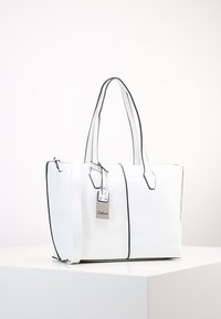 Witte tote bag met zwarte accenten, gestructureerd ontwerp, dubbele handvaten, ritssluiting en een zilveren label met "Gabor." Gladde textuur.