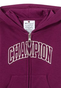 Felpa con zip viola realizzata in tessuto morbido, con logo bianco "CHAMPION" sul petto, due tasche anteriori e cappuccio.