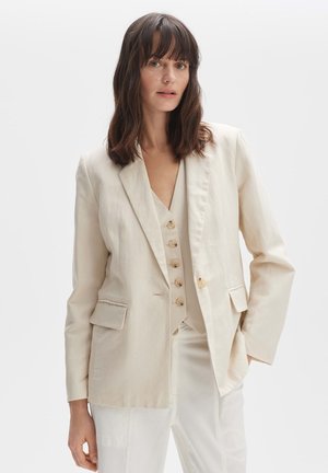 Beige Leinenblazer mit Reverskragen, zwei aufgesetzten Taschen, Ein-Knopf-Verschluss, über einem passenden Weste mit Holzknöpfen getragen.