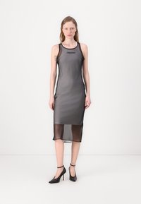 Schwarzes ärmelloses Kleid mit durchscheinendem Überzug, knielange Länge, taillierter Oberteil. Verfügt über ein Logo auf der Brust und eine glatte, leichte Textur.