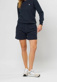 Sweat-shirt marine à manches longues avec un petit logo sur la poitrine, accompagné deShorts marine assortis. Baskets blanches avec des accents gris.