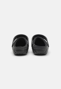 Zoccoli neri con cinturino posteriore regolabile, design testurizzato, interno imbottito e suola con motivo per una migliore aderenza.