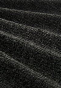 Schwarzer strukturierter Stoff mit einem gewebten Muster, das gewelltes Falten zeigt, die Tiefe und visuelles Interesse schaffen. Weicher, warmer Eindruck.