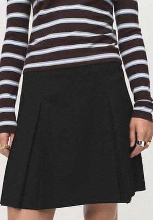 Jupe noire plissée avec une texture lisse; associée à un haut à manches longues rayé marron et bleu clair. Accessoires comprenant des bagues.