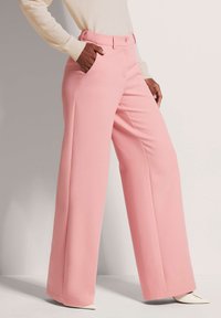 Zachte roze wijde broek met een gladde textuur, voorzien van zijzakken en een sluiting met een voorknoop, gestyled met een lichtbeige sweater.