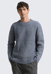 Grauer strukturierter Pullover mit Rundhalsausschnitt und gerippten Bündchen. Der Stoff weist ein gewebtes Muster auf, das ein gemütliches, grob gestricktes Aussehen verleiht.