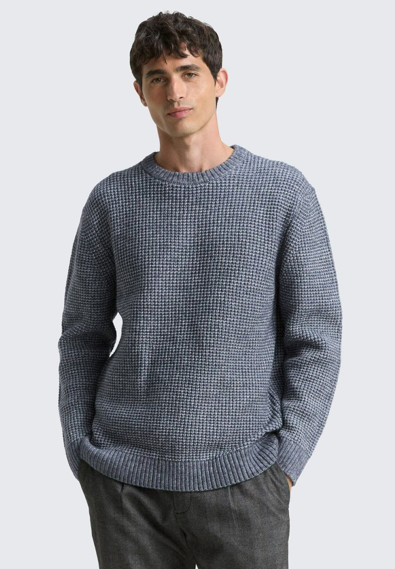 Grauer strukturierter Pullover mit Rundhalsausschnitt und gerippten Bündchen. Der Stoff weist ein gewebtes Muster auf, das ein gemütliches, grob gestricktes Aussehen verleiht.