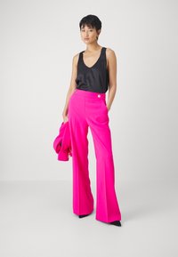 Pantaloni larghi rosa con vita alta e dettagli in oro, abbinati a un top in satin nero. Tessuto morbido, design strutturato.