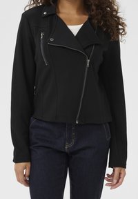 Černá přiléhavá bunda s krátkým střihem, asymetrickými zipy a kovovými ozdobami. Vyrobena z hladké pružné látky.