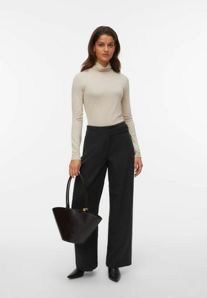 Polo hals met lange mouwen in beige, op maat gemaakte donkere broek, zwarte puntige schoenen en een donkere leren handtas in een driehoekige vorm.