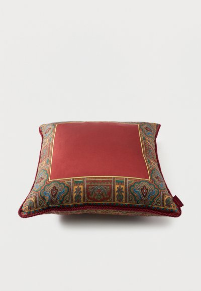 Coussin décoratif carré avec un centre rouge profond et une bordure cachemire multicolore complexe sur un fond clair.