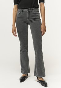 Jeans de mezclilla grises acampanados, con cintura alta, cinco bolsillos y un sutil deslavado. Combinados con bailarinas negras de punta.