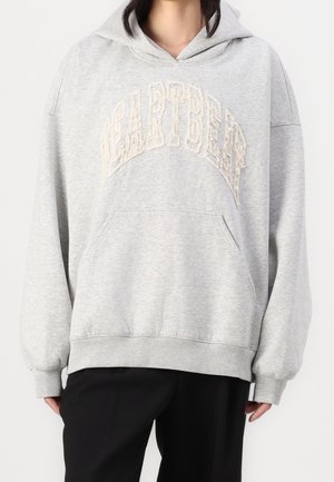 Persoon draagt een lichtgrijze capuchontrui met de getextureerde tekst "PEARTBEAR" en een kangeroezak aan de voorkant, gecombineerd met een zwarte broek.