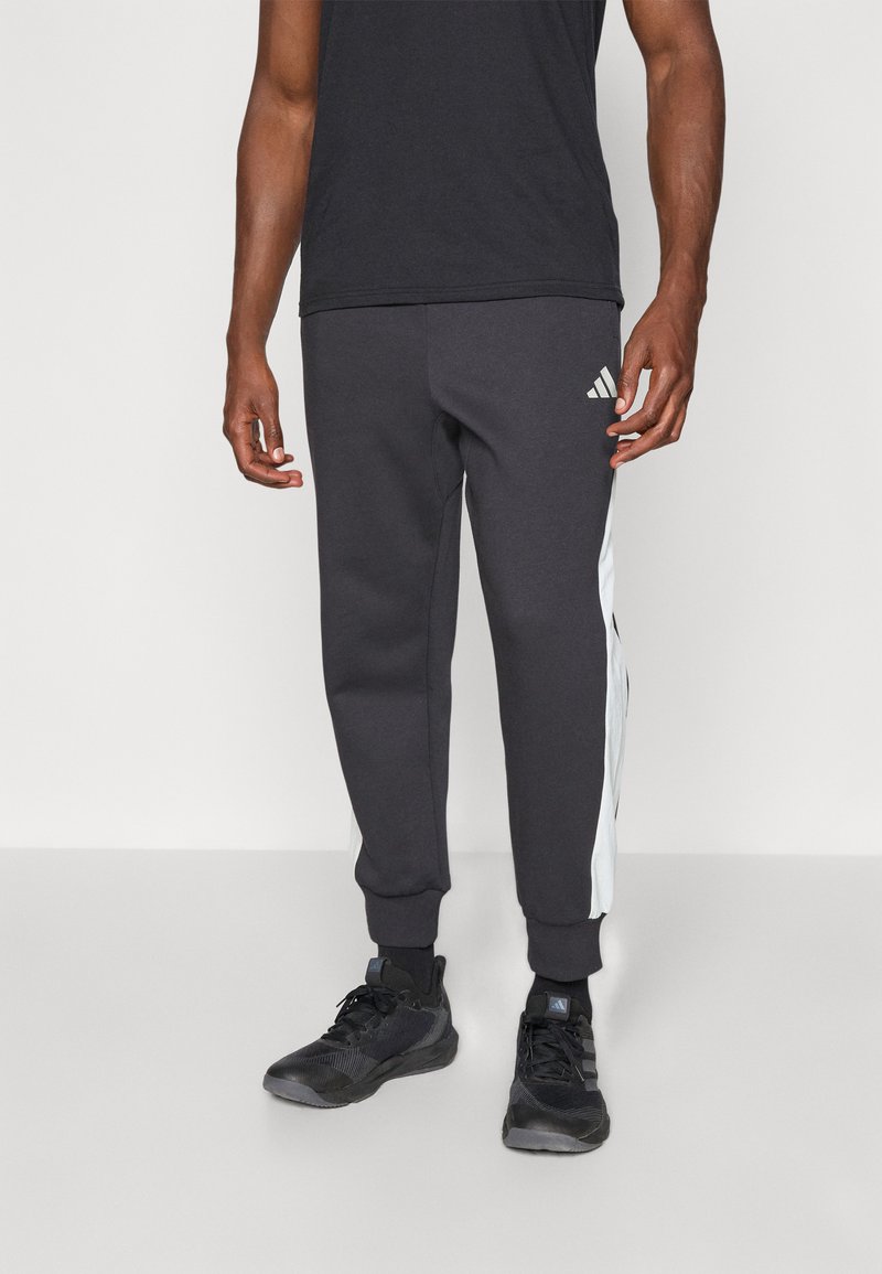 Węgorzowe szare spodnie dresowe z białymi paskami po bokach, z elastycznym paskiem w talii i mankietami. Logo Adidasa na dolnej lewej nodze.