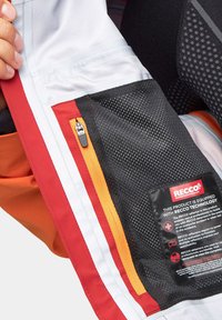 Kurtka wodoodporna w połączeniu pomarańczowego, białego i czarnego materiału. Posiada siatkową kieszeń i metkę z technologią RECCO.