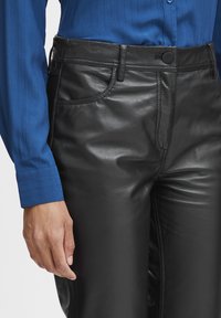 Zwarte leren broeken met een gladde textuur. Kenmerken zijn onder andere voorzakken, een enkele knoopsluiting en stiksels. Gekocht met een blauwe shirt.