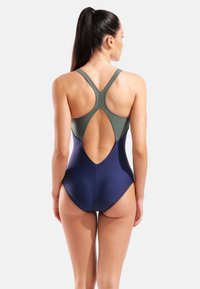 Bañador de una pieza en azul oscuro y verde oliva, con diseño cruzado en la espalda, espalda descubierta y tejido liso y elástico.