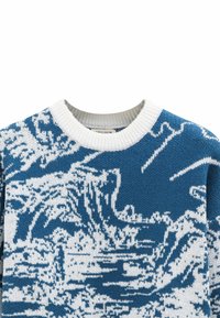 Pull en tricot bleu et blanc avec un motif de vagues, col rond et bordures côtelées. La texture semble douce et chaude.