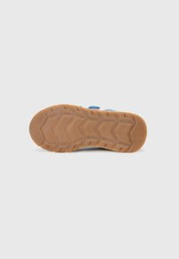 Semelle en caoutchouc avec un motif de semelle en zigzag, comportant des accents bleu clair sur une chaussure grise. Texture lisse avec un bout arrondi et des sangles ajustables.